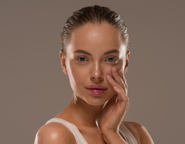 Beauty portrait of glowing skin in a white tank top showcasing face massager tools.